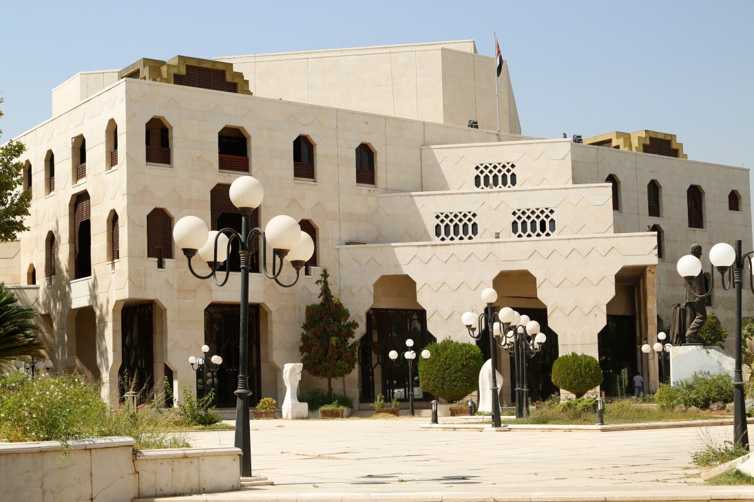 A large modern building with traditional Islamic architectural details on a sunny plaza.