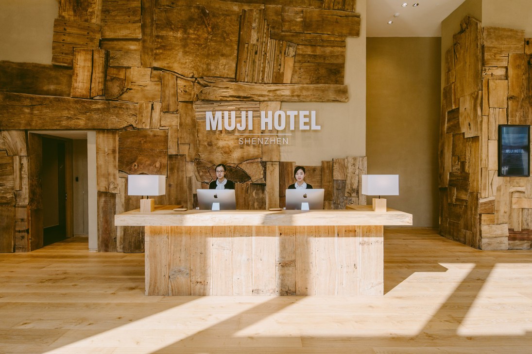 Muji Hotel Shenzhen reception desk with reclaimed wood wall paneling and two staff members at computers.