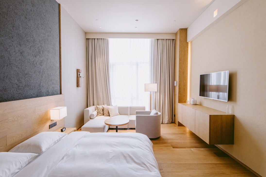 Minimalist Muji Hotel room with light wood furnishings, white bedding, neutral textiles, and clean-lined furniture.