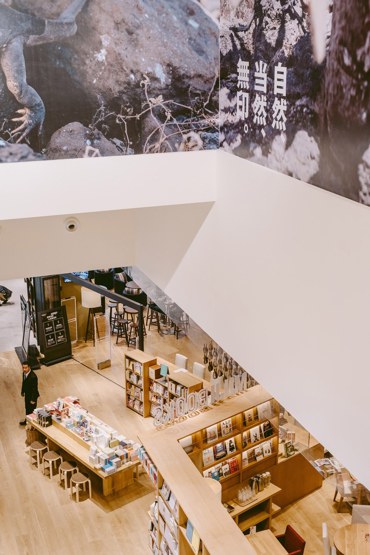 Overhead view of a multi-level Muji flagship store with light wood flooring, display tables, shelving, and a customer browsing merchandise.