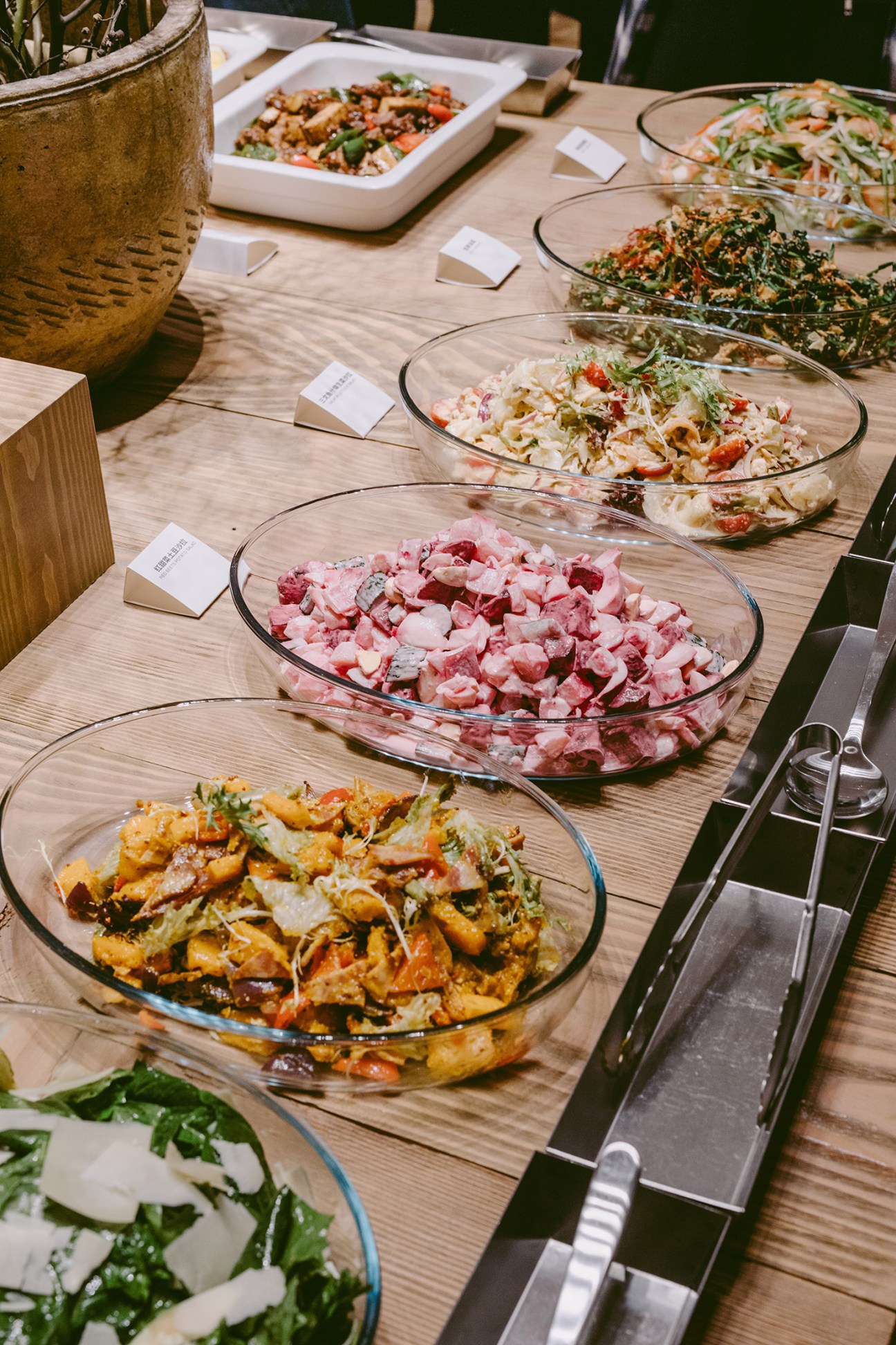 Multiple glass bowls of colorful Asian dishes arranged on a wooden table at Muji Hotel restaurant.