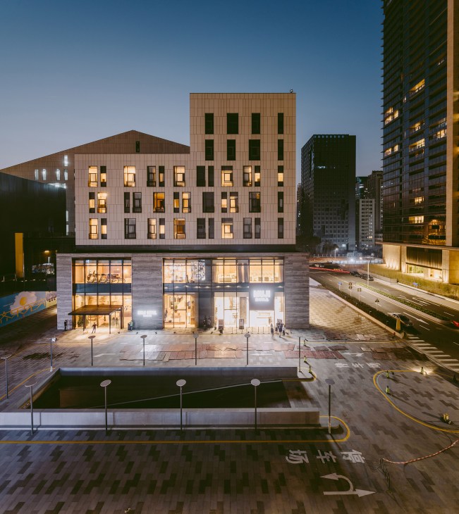 Muji Hotel exterior in Shenzhen at dusk, showing minimalist architecture with brown and cream facades, ground-floor retail space, and surrounding urban towers.