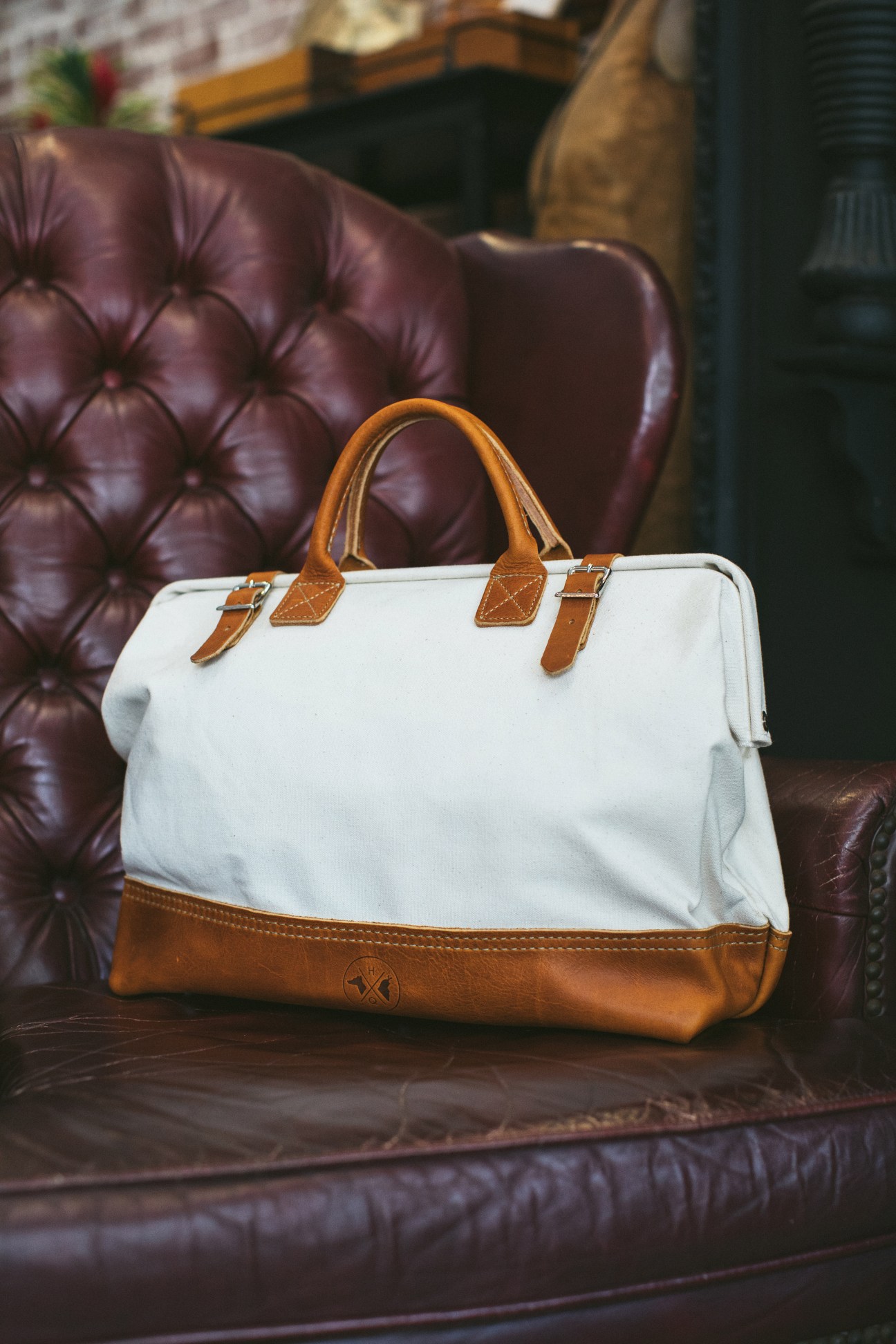 Hound and Quail's canvas-and-leather tote bag displayed on a burgundy leather chair.