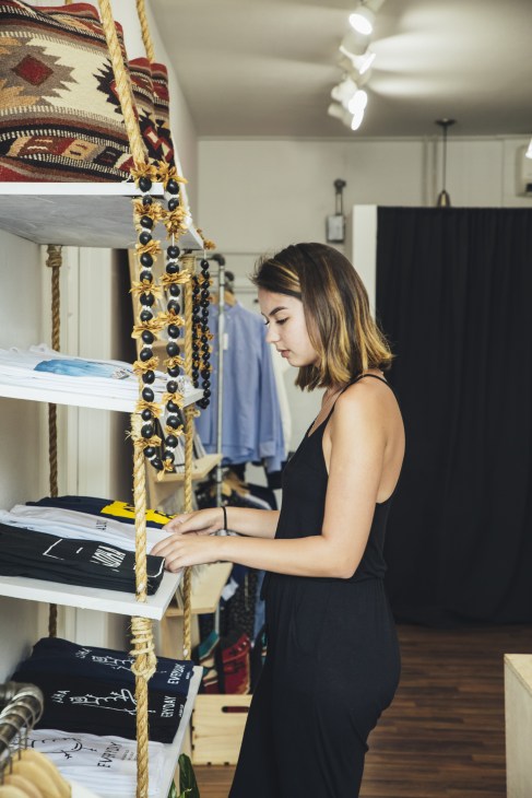 Woman examining fabric swatches and decorative beaded trim hanging on display shelves.