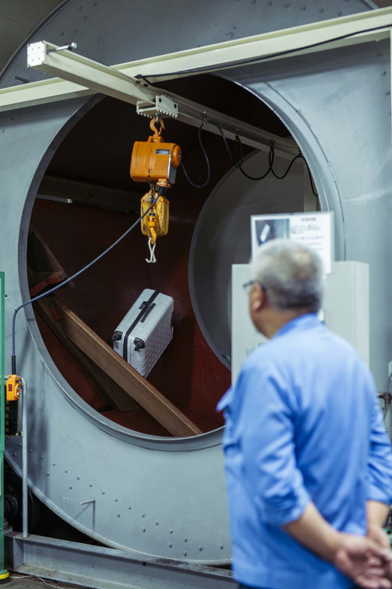 Ace suitcase being tested in quality control torture room with worker in blue shirt observing