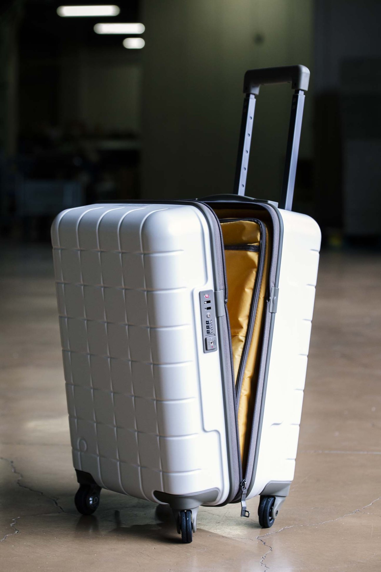 White Ace Proteca suitcase with open lid revealing gold interior lining in a factory setting