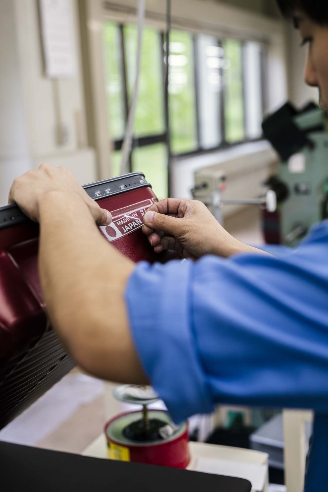 Quality control inspector examining a burgundy Ace suitcase with 'Made in Japan' label in manufacturing facility