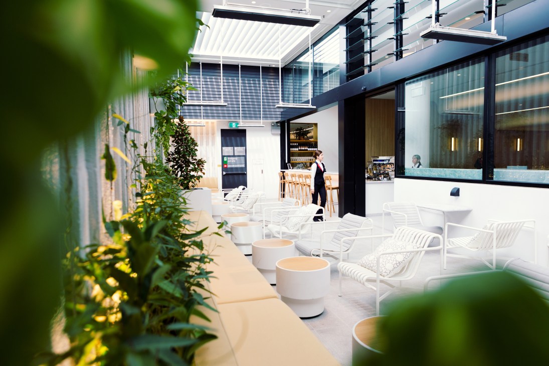 Perth International Airport transit lounge with green plants, white chairs, skylight, and outdoor bar area.
