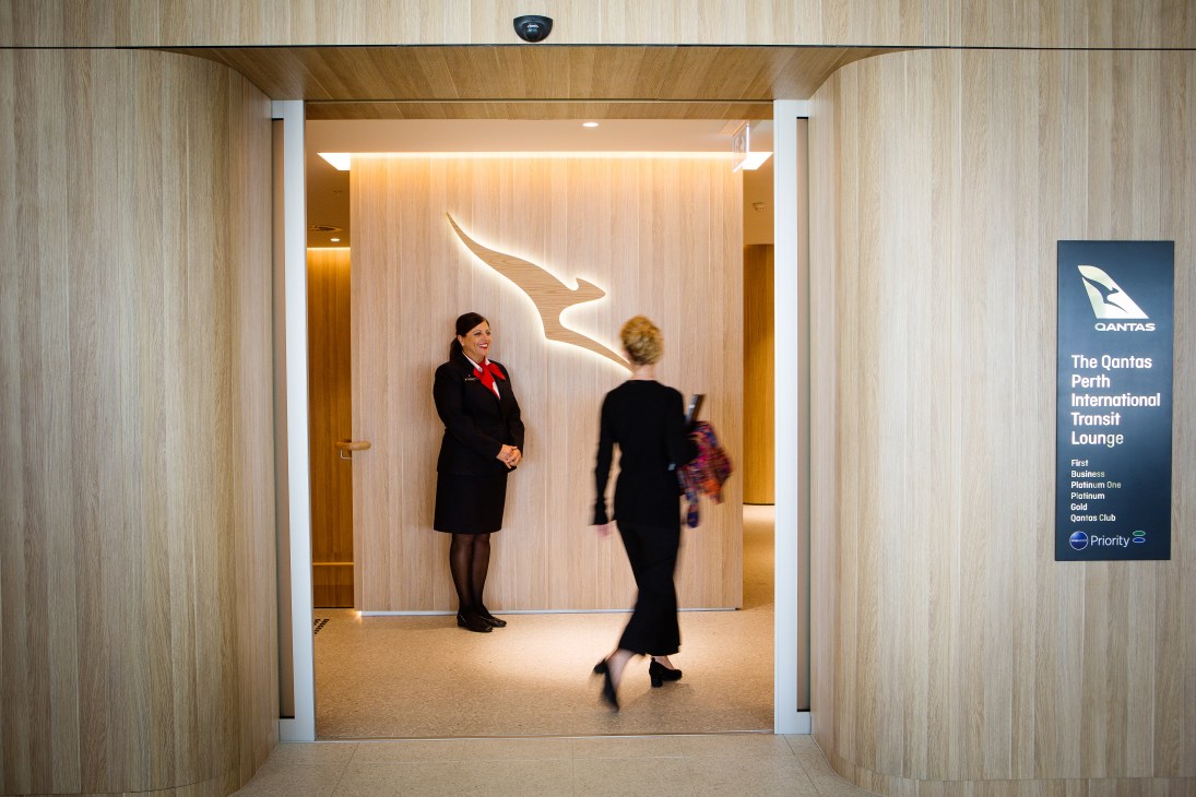 Interior of Perth International Transit Lounge with Qantas staff and illuminated kangaroo logo on wall.