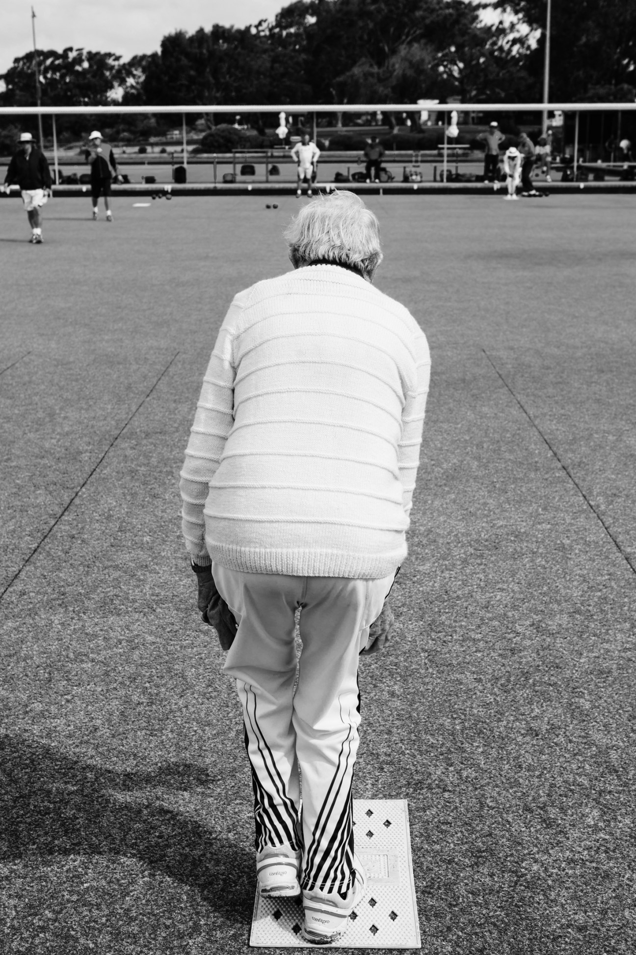 Elderly person in striped sweater playing lawn bowls on court