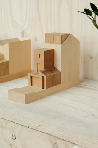 Wooden architectural model with geometric blocks in two different wood tones on white surface