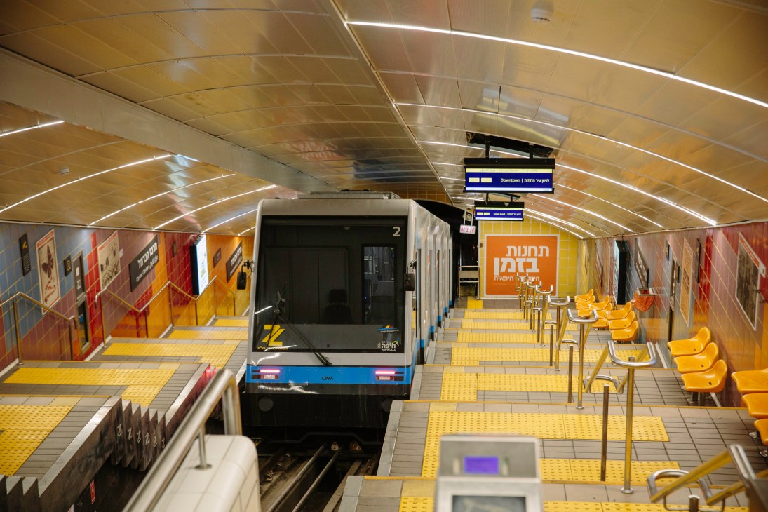 Interior of Haifa's underground funicular station with yellow seating and directional signage.