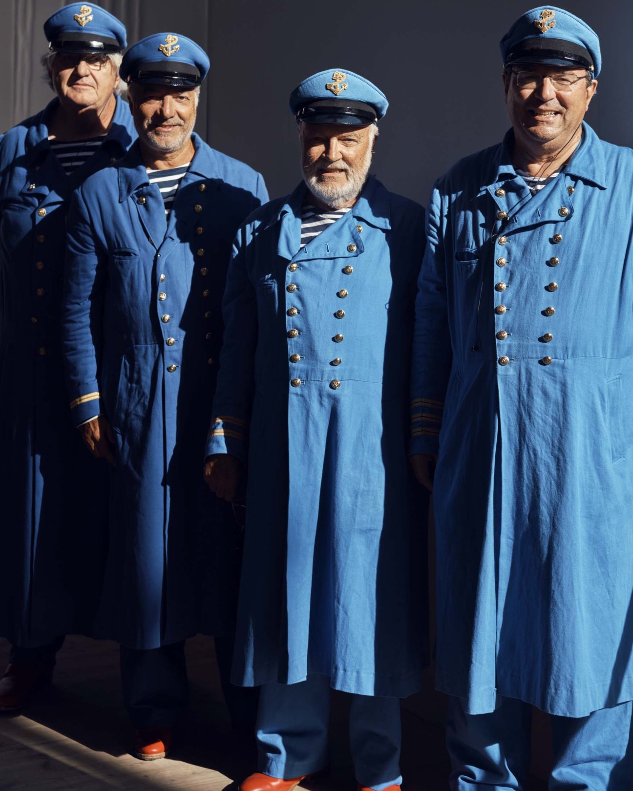 Four men in blue sailor uniforms with caps and striped shirts standing together outdoors