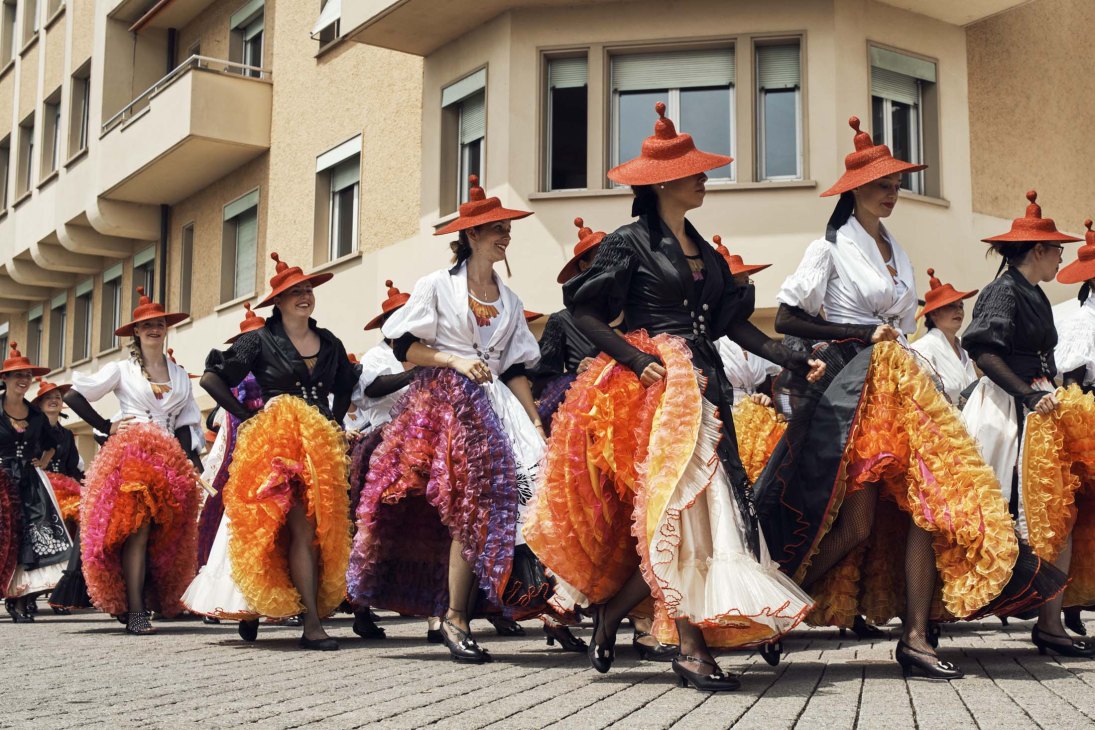 Can-can dancers in vibrant orange and red ruffled skirts performing on a city street