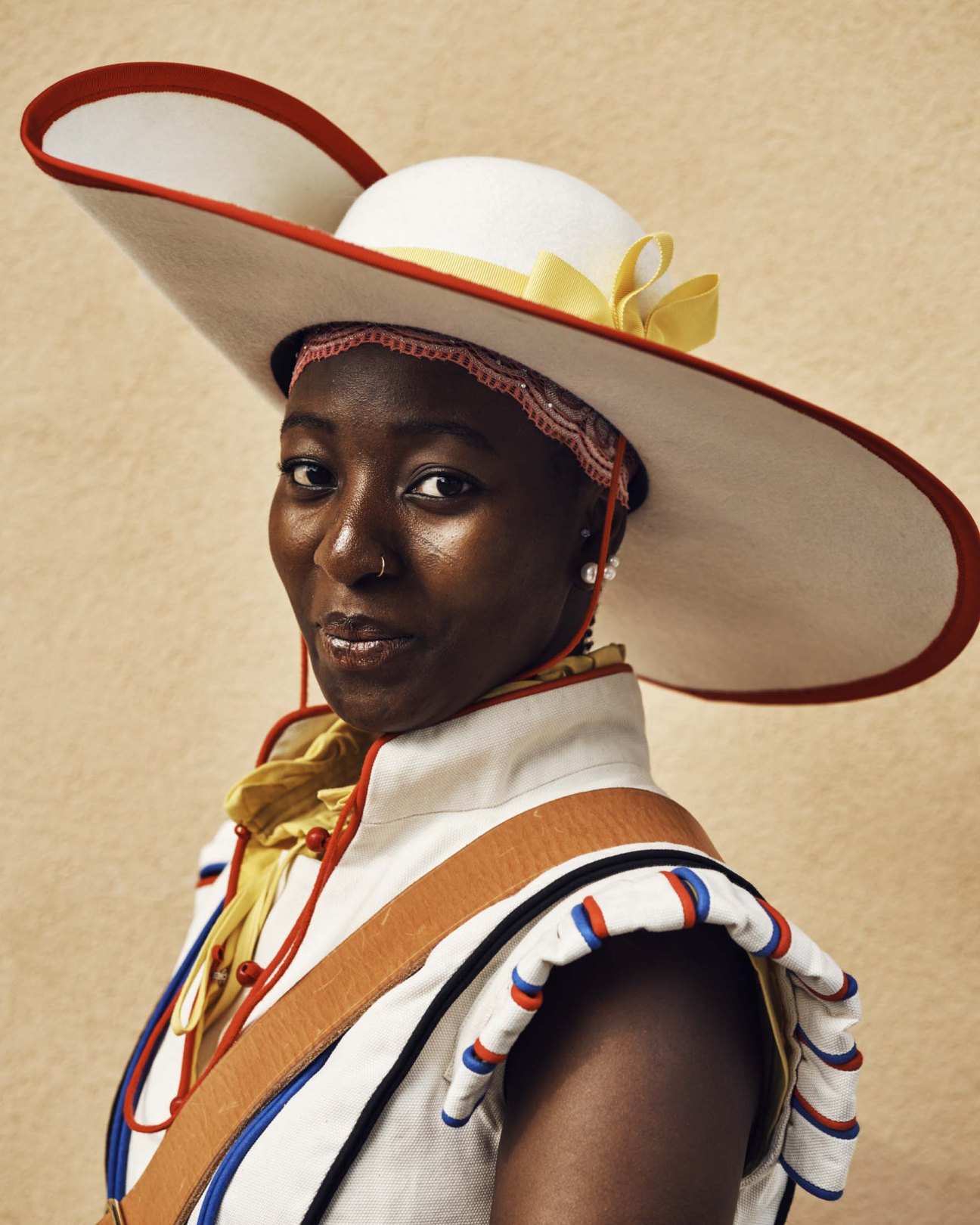 Woman in light cream and red military-style costume with wide-brimmed hat and yellow ribbon bow
