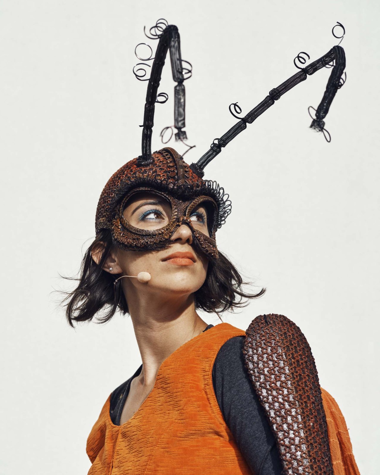 Person in brown textured costume with elaborate black mechanical headpiece featuring coiled springs and rings.