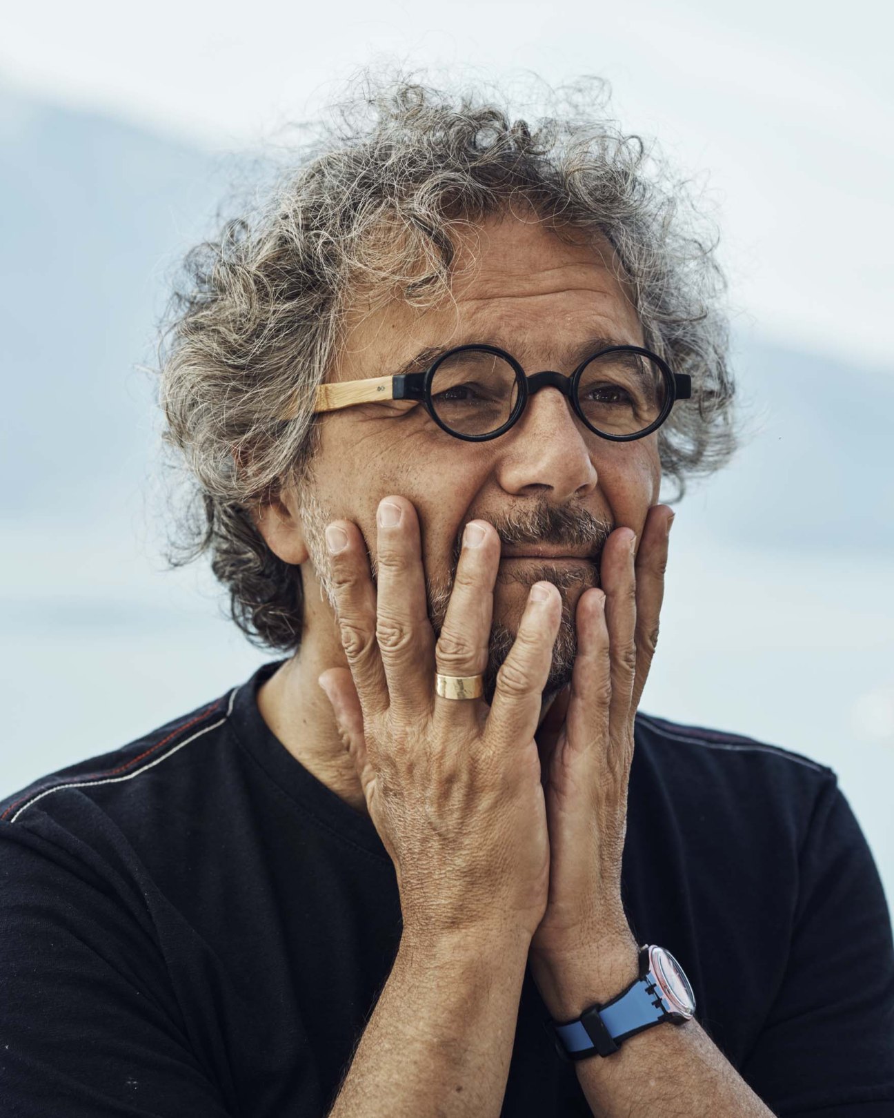 Director Daniele Finzi Pasca in black shirt and round glasses with hand to face outdoors