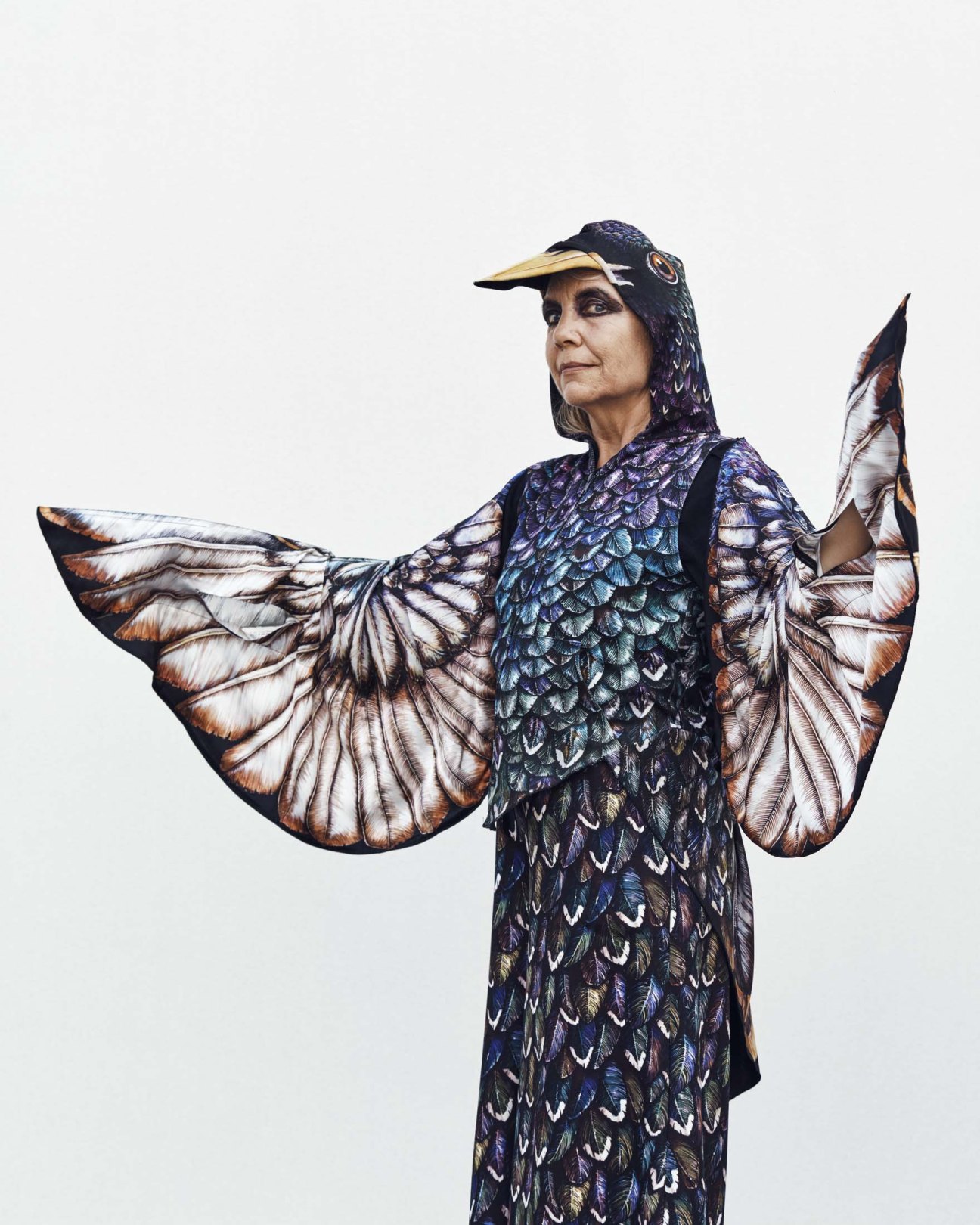 Woman in elaborate bird-wing festival costume with patterned dress and cap.