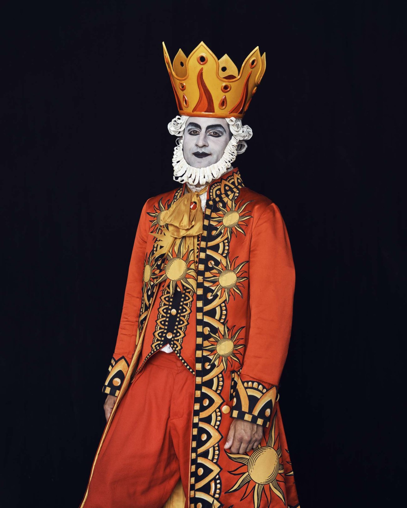 Male performer in royal costume with ornate red coat, white ruffled collar, and golden flame crown portraying King David