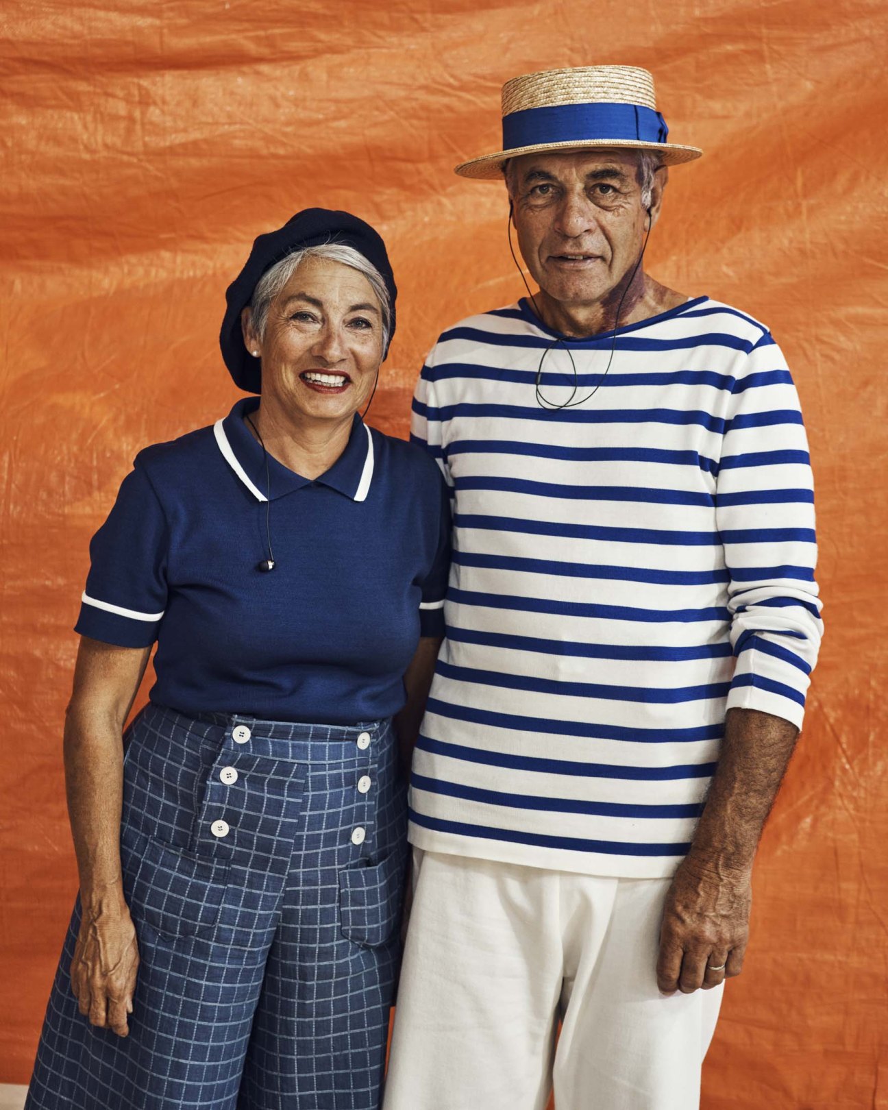 Two older adults in vintage nautical-inspired costumes posing against an orange backdrop.
