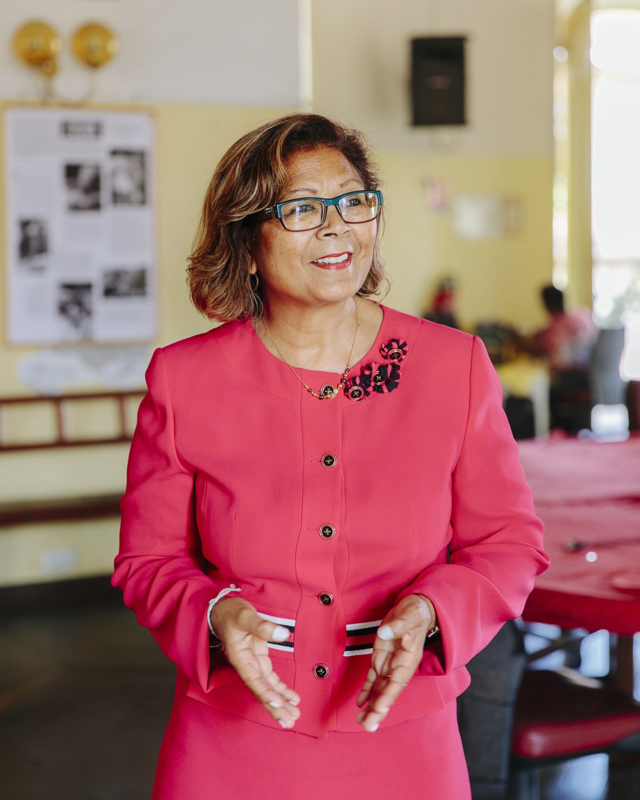 Cayenne's mayor Marie-Laure Phinéra-Hort in a bright pink blazer and blue glasses standing in an official interior.