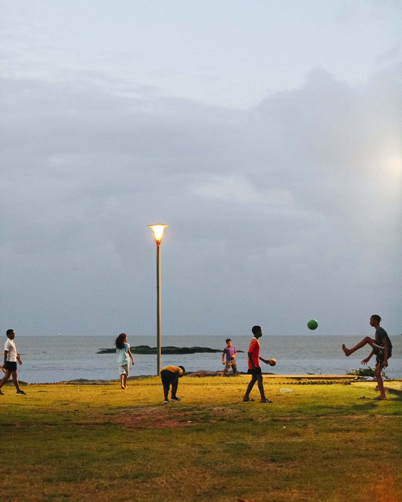 Children playing with a ball on Amandiers Beach in French Guiana under overcast skies.