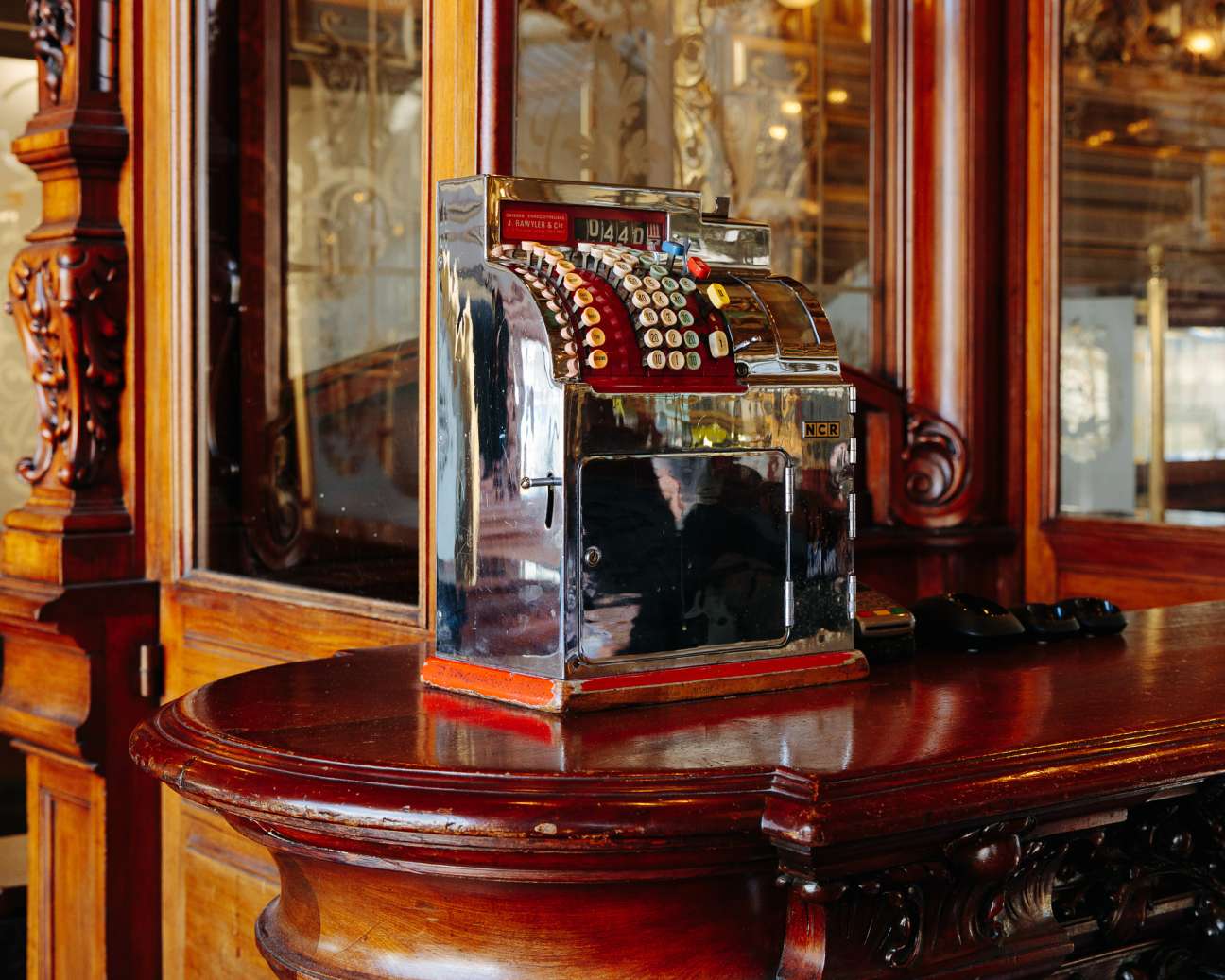 Vintage NCR cash register with red and gold detailing on a wooden table at Le Train Bleu restaurant.