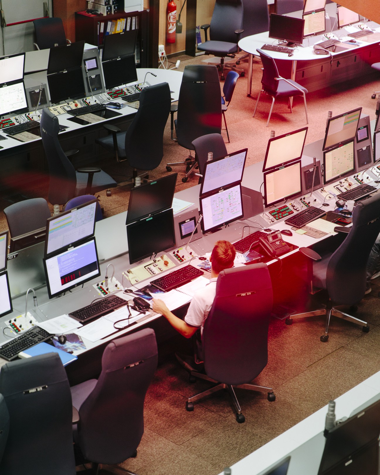 Control room at Kourou Space Centre with multiple workstations, monitors displaying data, and an operator in a red chair.