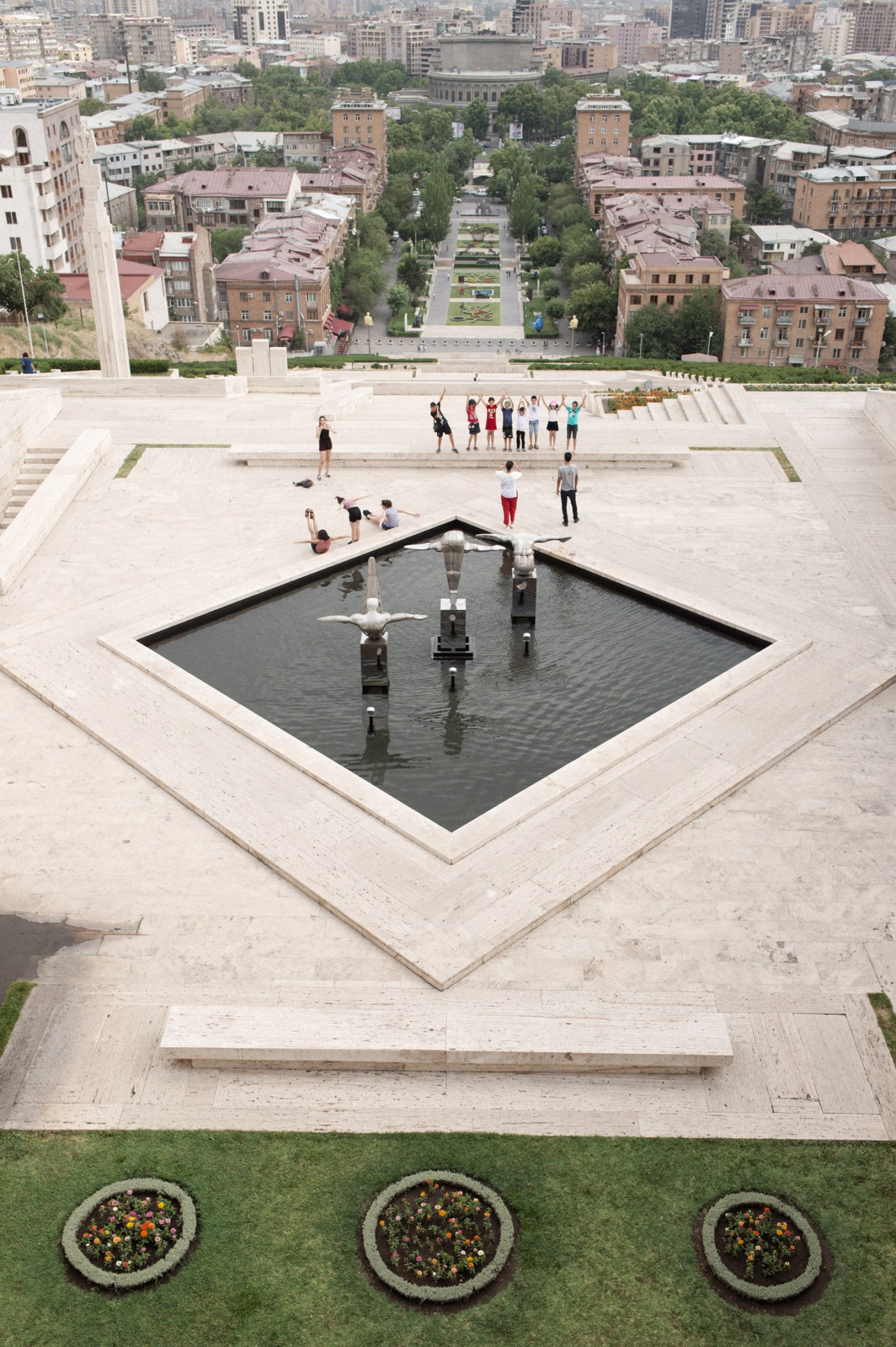 Tourists posing on The Cascade structure in Yerevan, mimicking a diving sculpture overlooking the city.