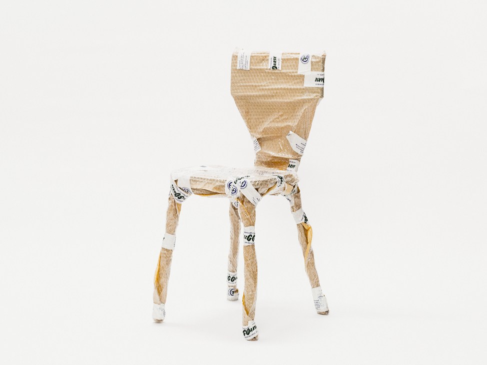 A chair constructed from kraft paper wrapping and labeled tape, displayed against a white background.