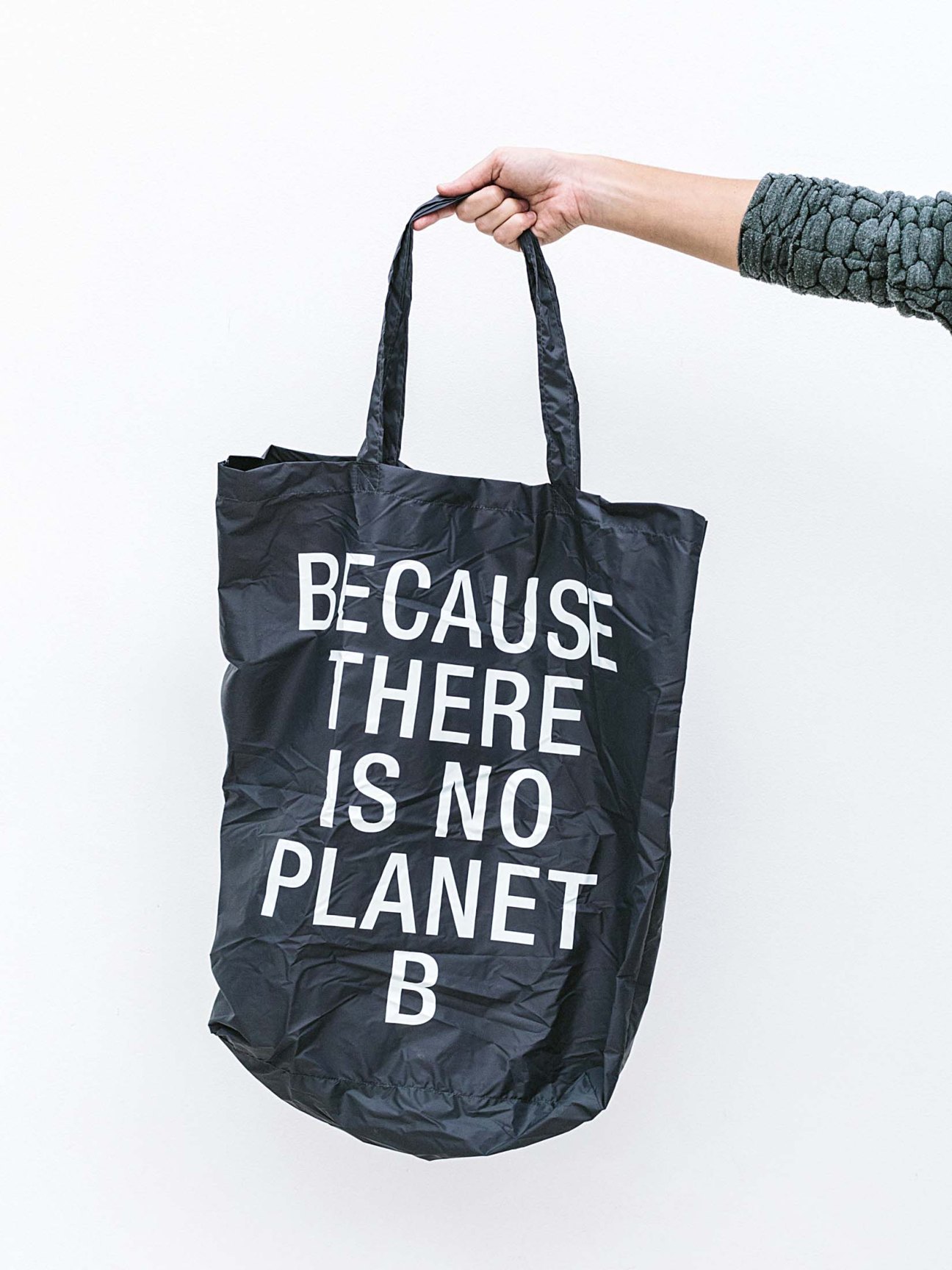Hand holding a black Ecoalf tote bag made from recycled materials with "BECAUSE THERE IS NO PLANET B" text