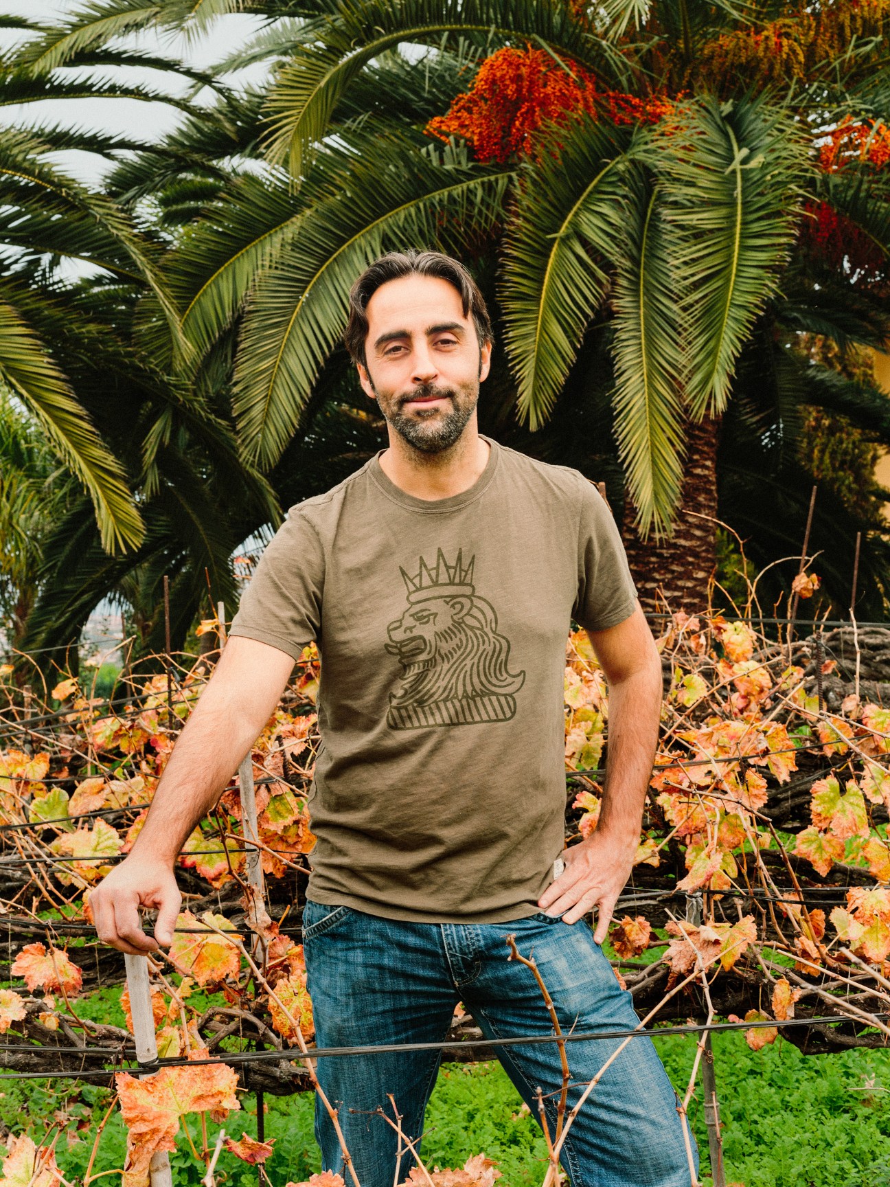 Jonatan García Lima, winemaker and owner of Suertes del Marqués, stands among palm trees and autumn foliage in Tenerife vineyards.