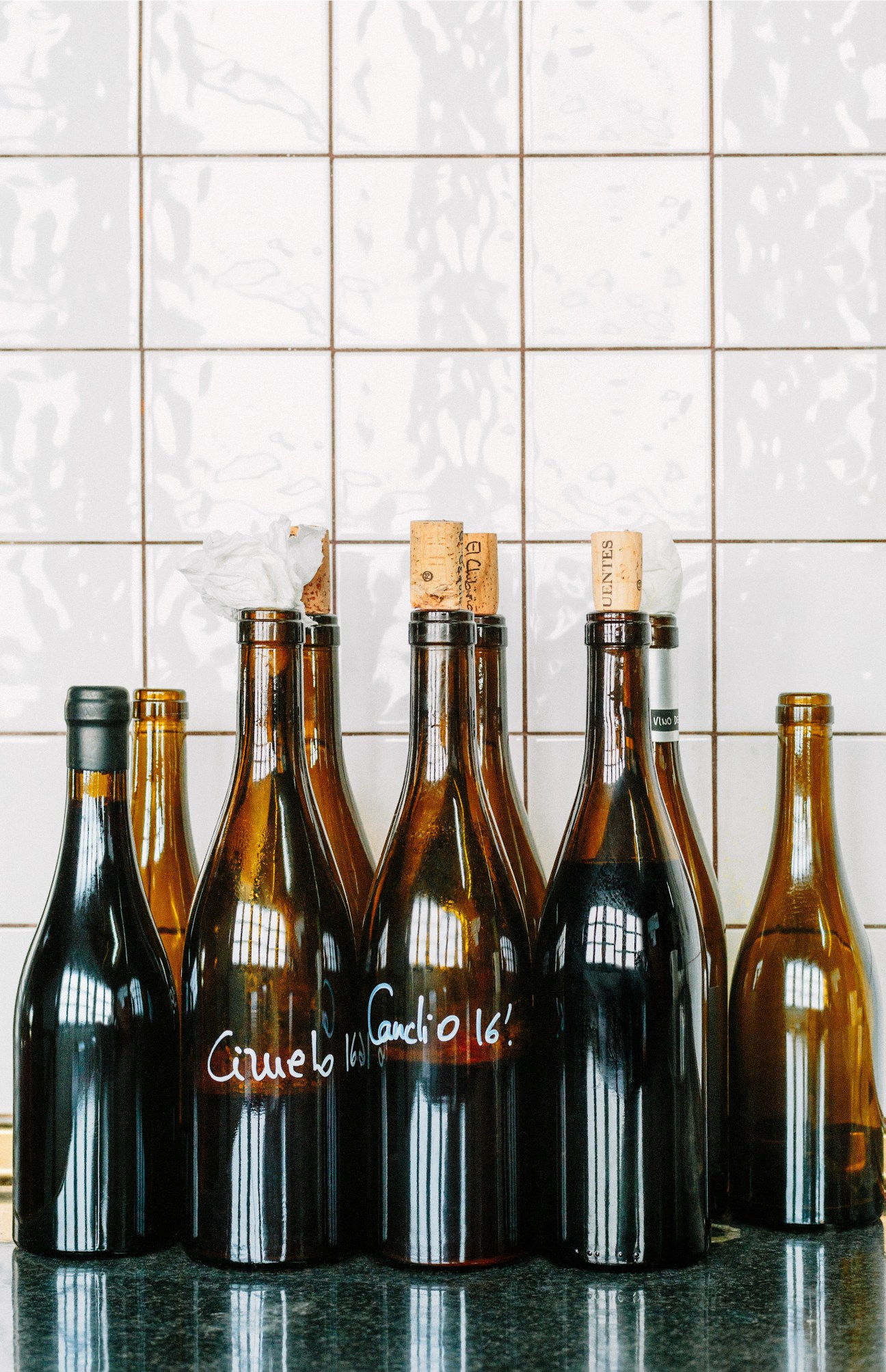 Test bottles of wine at Suertes del Marqués winery with cork stoppers and cloth covers against white tiles.
