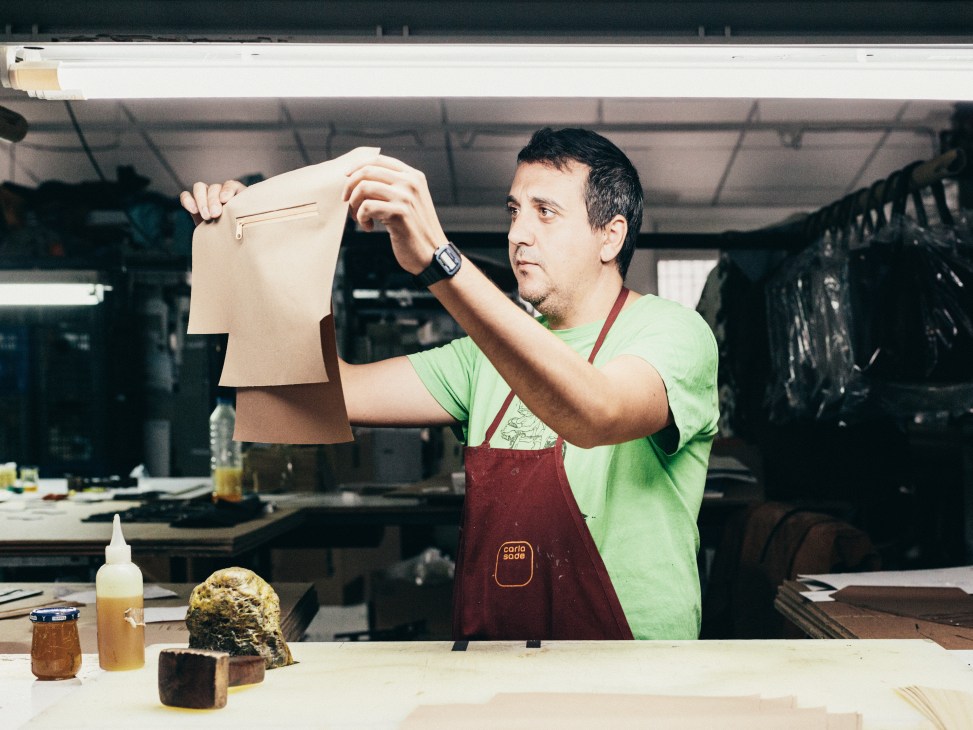 Leather craftsman inspecting a cream-colored hide at Carla Sade factory workstation.