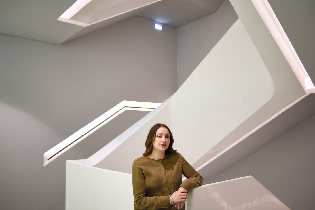 Katerina Georgopoulou stands in a modern, minimalist interior space with angular white architectural elements and skylights.