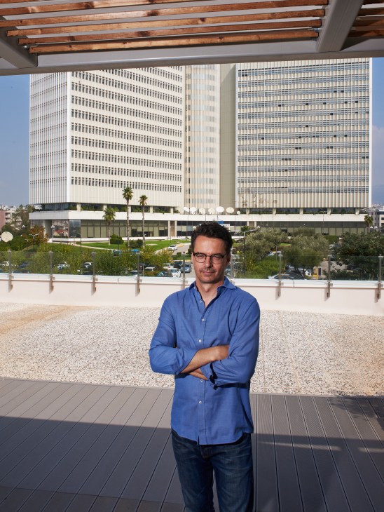 Michalis Rikakis, computer engineer at Workable, standing on a rooftop terrace in Athens with modern buildings behind him.