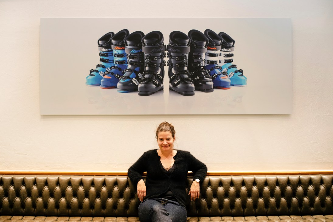 CEO Olivia Strolz sits on a leather banquette beneath a display of custom Strolz ski boots in various colors.