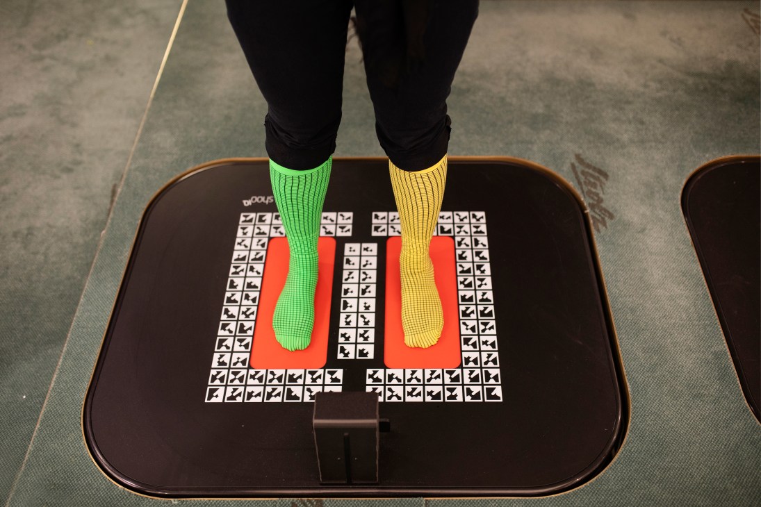 Person wearing neon green and yellow socks stands on a 3D foot scanner platform used for custom ski boot fitting.