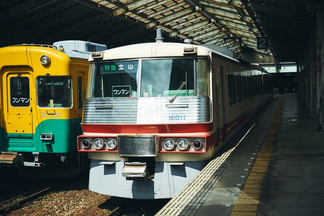 Japanese trains parked at a railway station platform under a glass roof structure.