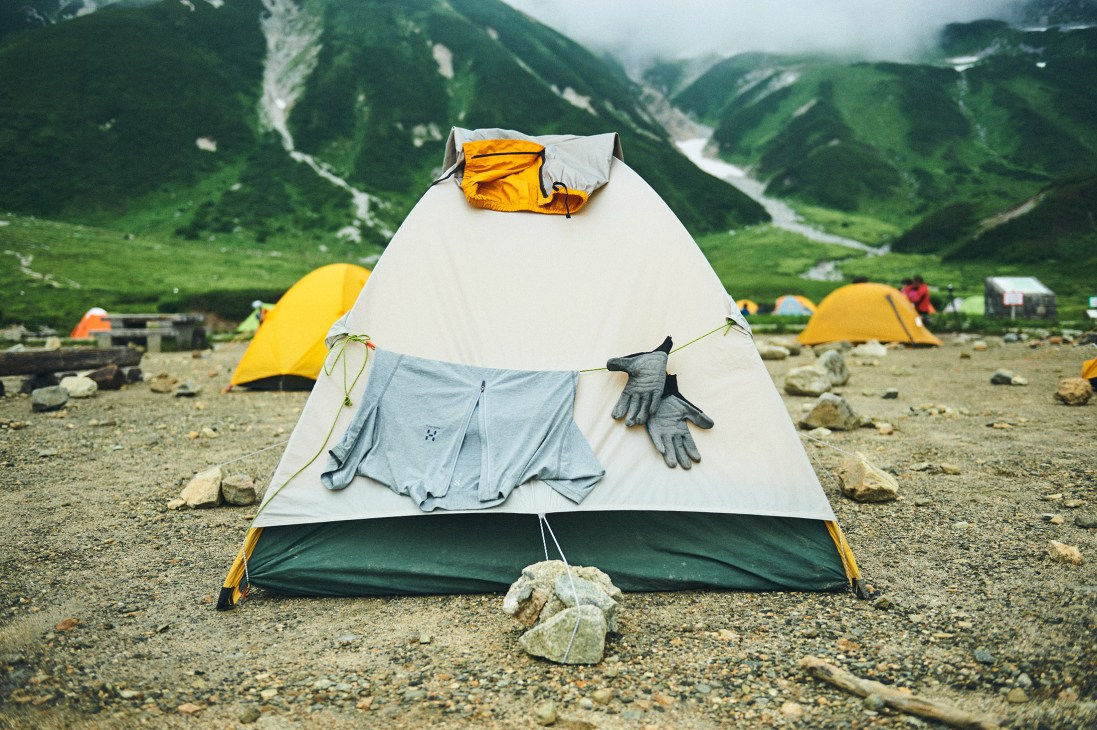 Hiking clothes and gloves drying on a tent at a mountain campsite with verdant valleys visible beyond.