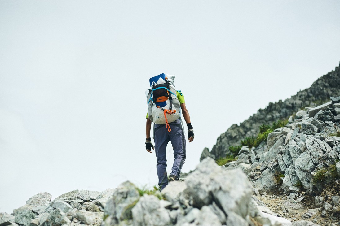 Hiker with colorful backpack and gear trekking solo along rocky mountain ridge trail.