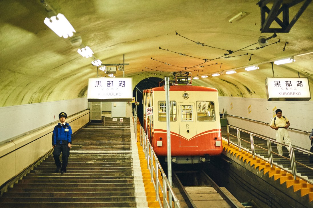 Underground cable car station at Kurobeko with red and cream train and workers on platform.