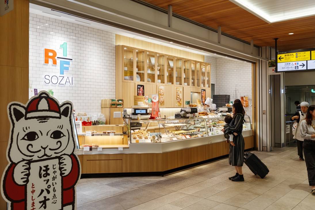 Customer browsing glass display case at deli counter in modern Japanese station retail space