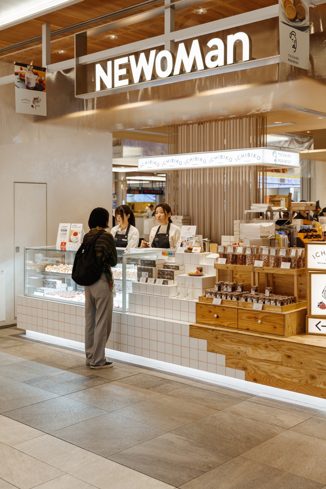 Customer browsing at a CHIBIKO bakery counter inside Newoman mall with staff serving behind display cases