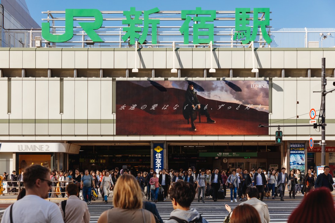 Crowds of people crossing a busy street in front of a large JR station building with green signage