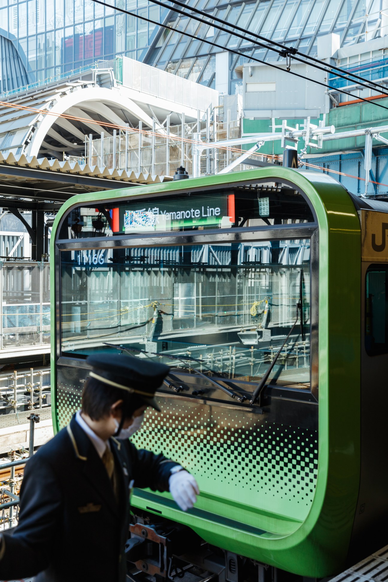 Train guard in uniform standing next to green Yamanote line train at Shibuya station