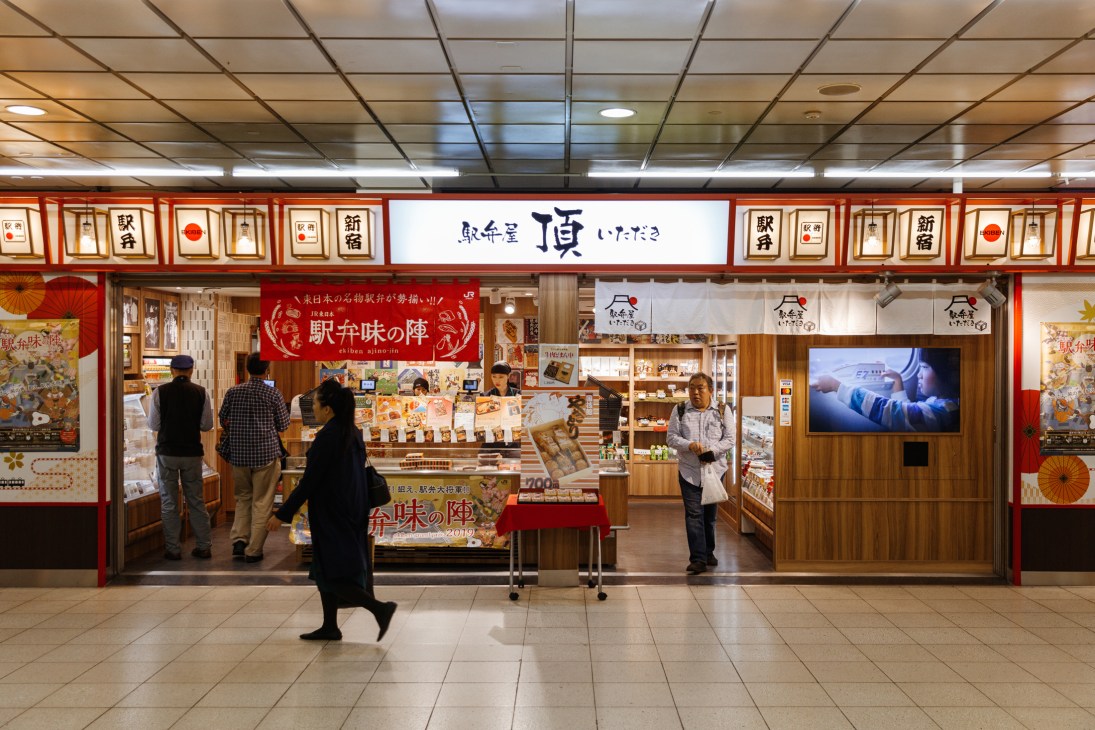 Japanese railway station shop with traditional red and white signage and customers browsing products