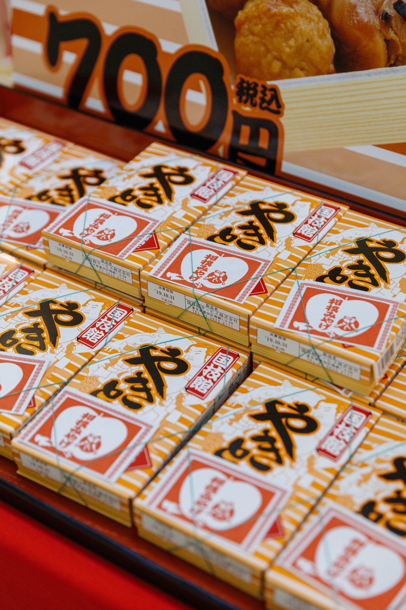 Orange and white snack boxes with Japanese text and 700 yen price tags displayed on retail shelves