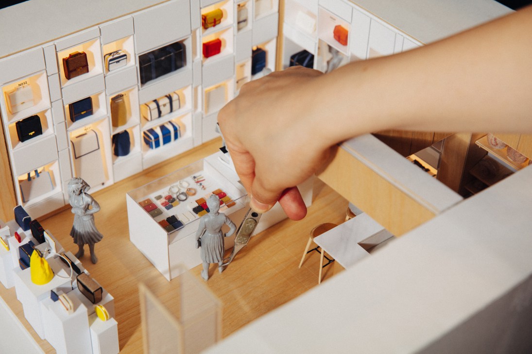 Hand reaching into miniature retail store model to adjust lighting and fixtures
