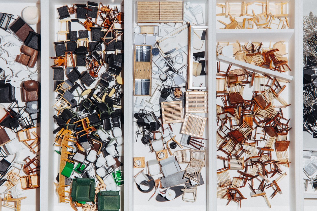 Organized compartments filled with miniature chairs in various colors and styles for architectural model-making